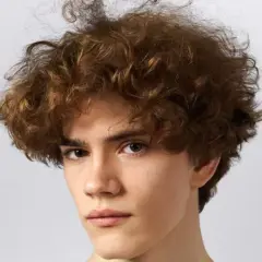 Primer plano de un joven con cabello rizado y castaño sobre fondo blanco.