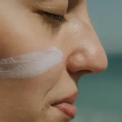 Protección solar: ¿SPF qué es? Crema blanca aplicada en la mejilla de una persona, con el mar al fondo.