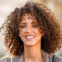 Mujer con rizos voluminosos y un estilo que evoca los peinados años 20. Su pelo rizado luce natural y lleno de vida.