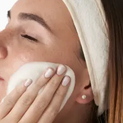 Mujer con diadema aplicándose espuma limpiadora en el rostro, parte de su rutina facial de noche.
