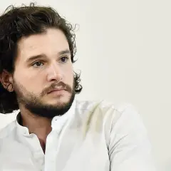 Hombre con pelo rizado oscuro y barba, viste camisa blanca.