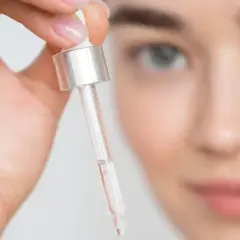 Mujer sosteniendo un gotero con líquido transparente cerca de su rostro.