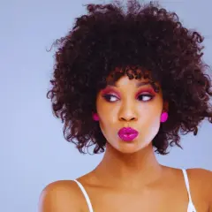Mujer con rizos chicos y maquillaje vibrante, jugando con un mechón de su cabello.