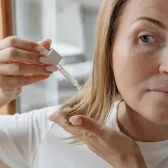 Mujer aplica aceite de argán en su pelo rizado. Gotas de aceite caen sobre su mano.