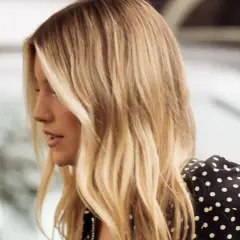 Perfil de mujer con cabello rubio mantequilla, ondas suaves y un vestido negro con lunares blancos.