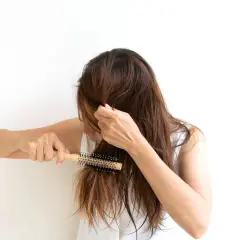 Mujer con cabello castaño se peina con un cepillo redondo, buscando un tratamiento para pelo que se rompe.