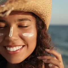 Mujer sonríe con protector solar en la cara, protegiéndose de la elastosis solar.