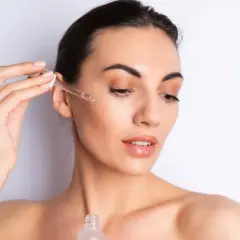 Una mujer aplica serum en su rostro con un gotero. Así se aplica el serum para una piel radiante.