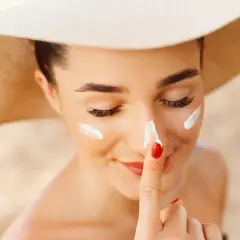 Mujer con sombrero de ala ancha se aplica protector solar en su piel blanca.