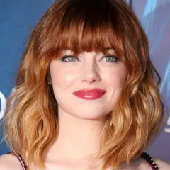 Emma Stone luce un vibrante pelo naranja en cascada, un estilo que realza su belleza natural.