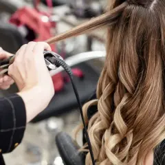 Manos expertas usando una tenaza para rizar el cabello rubio y castaño, creando ondas perfectas.