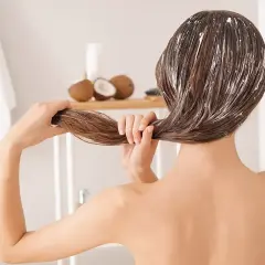 Mujer aplicándose mascarilla capilar con aceite de coco. Descubre para qué sirve el aceite de coco para un cabello radiante.