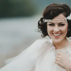 Novia sonriente con semirecogido pelo corto boda, diadema de perlas y encaje, velo vaporoso.