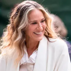 Mujer sonríe con cabello rubio y castaño con técnica reverse balayage, luciendo un abrigo blanco.