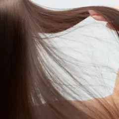 Mano acariciando su pelo fino y ondulado, de color castaño oscuro, que cae en cascada.