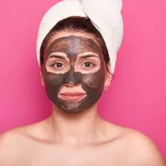 Una mujer con una toalla en la cabeza y una mascarilla de barro en la cara cansada, lista para un tratamiento de spa.
