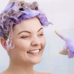 Sonrisa radiante con cabello teñido de violeta, lista para el antes y después. Guantes con espuma violeta.
