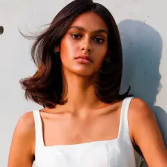 Mujer con cabello castaño brillante y piel bronceada, luciendo un vestido blanco. Su cabello parece suave, como si hubiera aprendido como se usa el acondicionador.