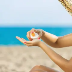 Mujer con sombrero aplicando crema solar en la mano. ¡No dejes que la crema solar caduca te arruine el día en la playa!