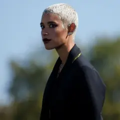 Mujer con pelo blanco corto y maquillaje dramático, luciendo un pendiente llamativo en la oreja.