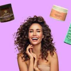 Mujer sonriente con rizos perfectos, rodeada de productos para el cabello: cremas, geles y espumas para definirlos.