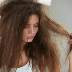 Mujer con pelo deshidratado, sin brillo y enredado, tocándose la cabeza con preocupación.