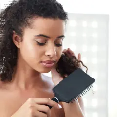 Mujer con pelo rizado y enredado, intentando desenredar con un cepillo negro.