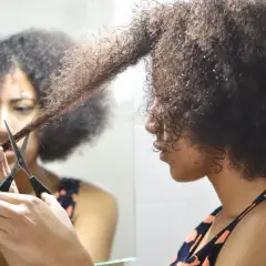 Mujer se corta el pelo rizado en casa, mirando su reflejo en el espejo.