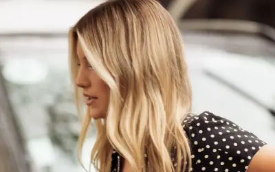 Perfil de mujer con cabello rubio mantequilla, ondas suaves y un vestido negro con lunares blancos.