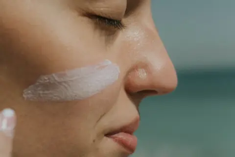 Protección solar: ¿SPF qué es? Crema blanca aplicada en la mejilla de una persona, con el mar al fondo.