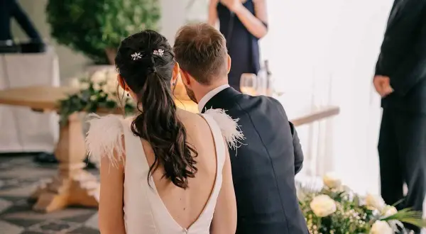 Novia con coleta baja adornada con horquillas, ideal para peinados para boda civil. El novio, de traje oscuro, la acompaña.