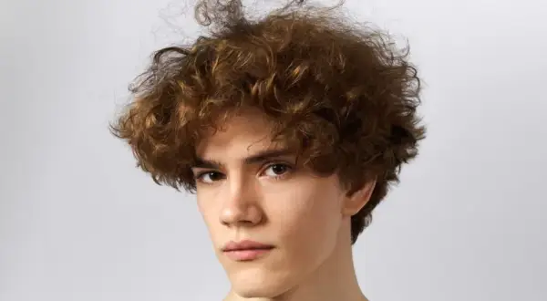 Primer plano de un joven con cabello rizado y castaño sobre fondo blanco.