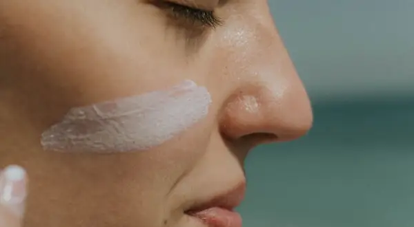 Protección solar: ¿SPF qué es? Crema blanca aplicada en la mejilla de una persona, con el mar al fondo.