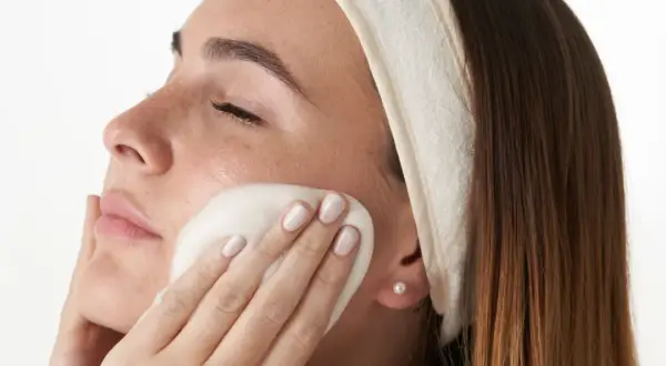 Mujer con diadema aplicándose espuma limpiadora en el rostro, parte de su rutina facial de noche.