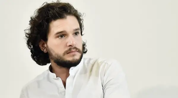 Hombre con pelo rizado oscuro y barba, viste camisa blanca.