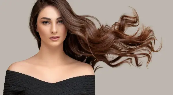 Mujer con cabello castaño ondulado y largo, con un vestido negro. ¿Buscas como quitar el tinte del pelo?
