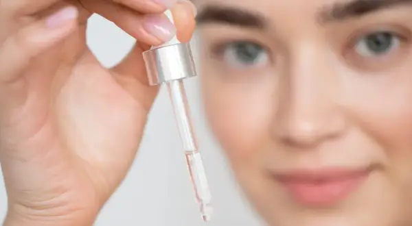 Mujer sosteniendo un gotero con líquido transparente cerca de su rostro.