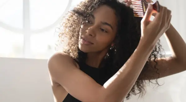 Mujer con pelo rizado cepillado en seco, peinando su cabello con un peine de dientes anchos.