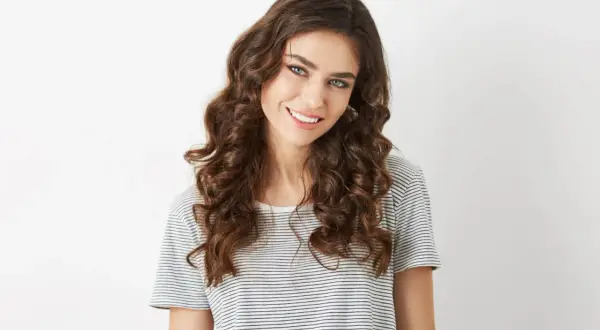Mujer sonriente con pelo ondulado castaño, ojos azules y camiseta a rayas.