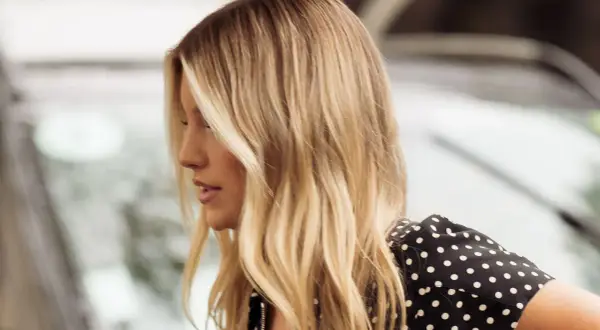 Perfil de mujer con cabello rubio mantequilla, ondas suaves y un vestido negro con lunares blancos.