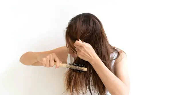 Mujer con cabello castaño se peina con un cepillo redondo, buscando un tratamiento para pelo que se rompe.