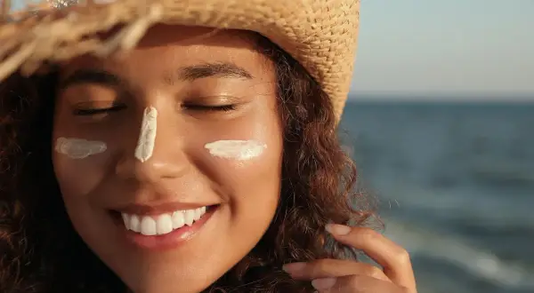 Mujer sonríe con protector solar en la cara, protegiéndose de la elastosis solar.