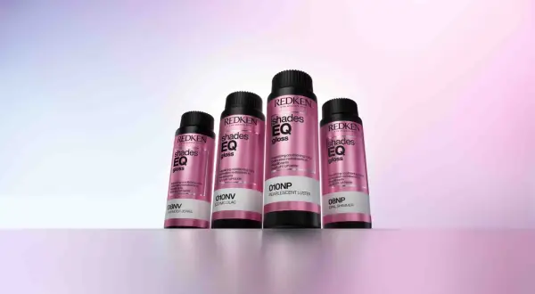 Cuatro botellas de baño de brillo para el pelo Redken Shades EQ Gloss en tonos perlados y lilas, listas para dar un acabado radiante.