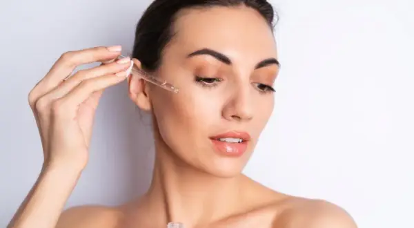 Una mujer aplica serum en su rostro con un gotero. Así se aplica el serum para una piel radiante.
