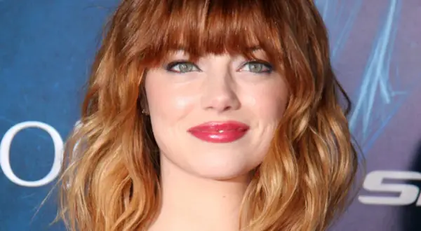 Emma Stone luce un vibrante pelo naranja en cascada, un estilo que realza su belleza natural.