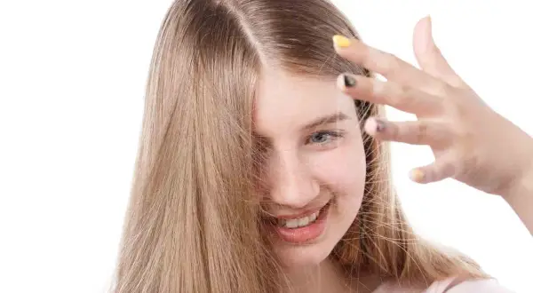 Chica sonriente con cabello rubio que se electrifica. Descubre cómo quitar la electricidad del pelo para un look suave.