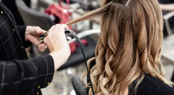 Manos expertas usando una tenaza para rizar el cabello rubio y castaño, creando ondas perfectas.