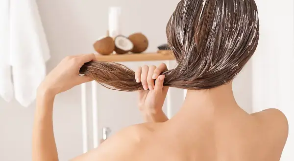 Mujer aplicándose mascarilla capilar con aceite de coco. Descubre para qué sirve el aceite de coco para un cabello radiante.