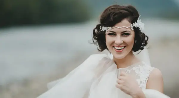 Novia sonriente con semirecogido pelo corto boda, diadema de perlas y encaje, velo vaporoso.