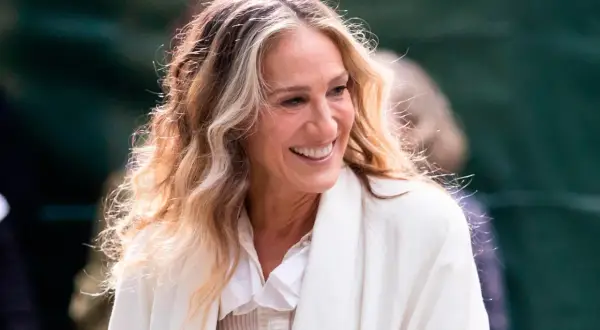 Mujer sonríe con cabello rubio y castaño con técnica reverse balayage, luciendo un abrigo blanco.